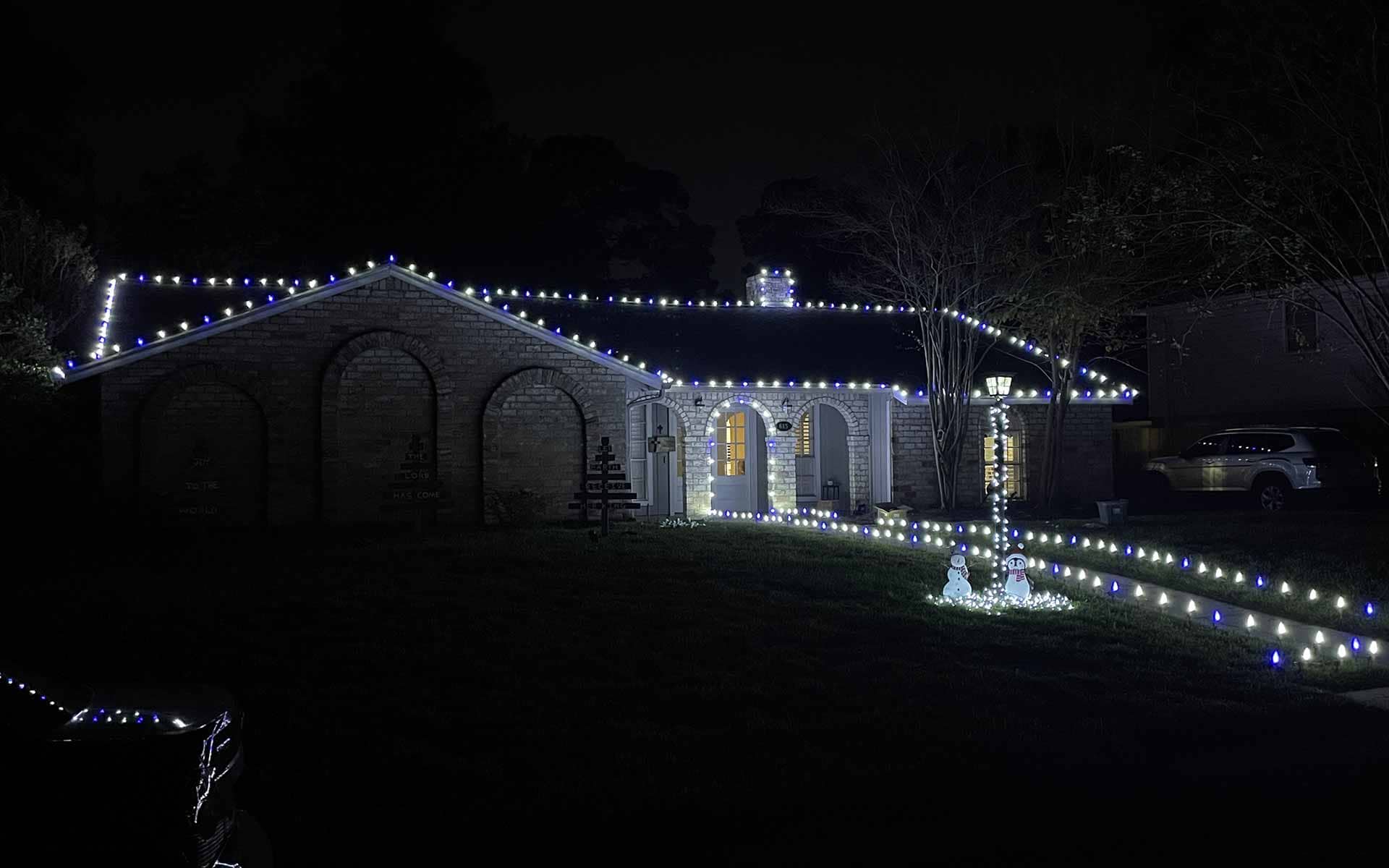 Blue and white Christmas lights outlining a brick home with a lit front walkway