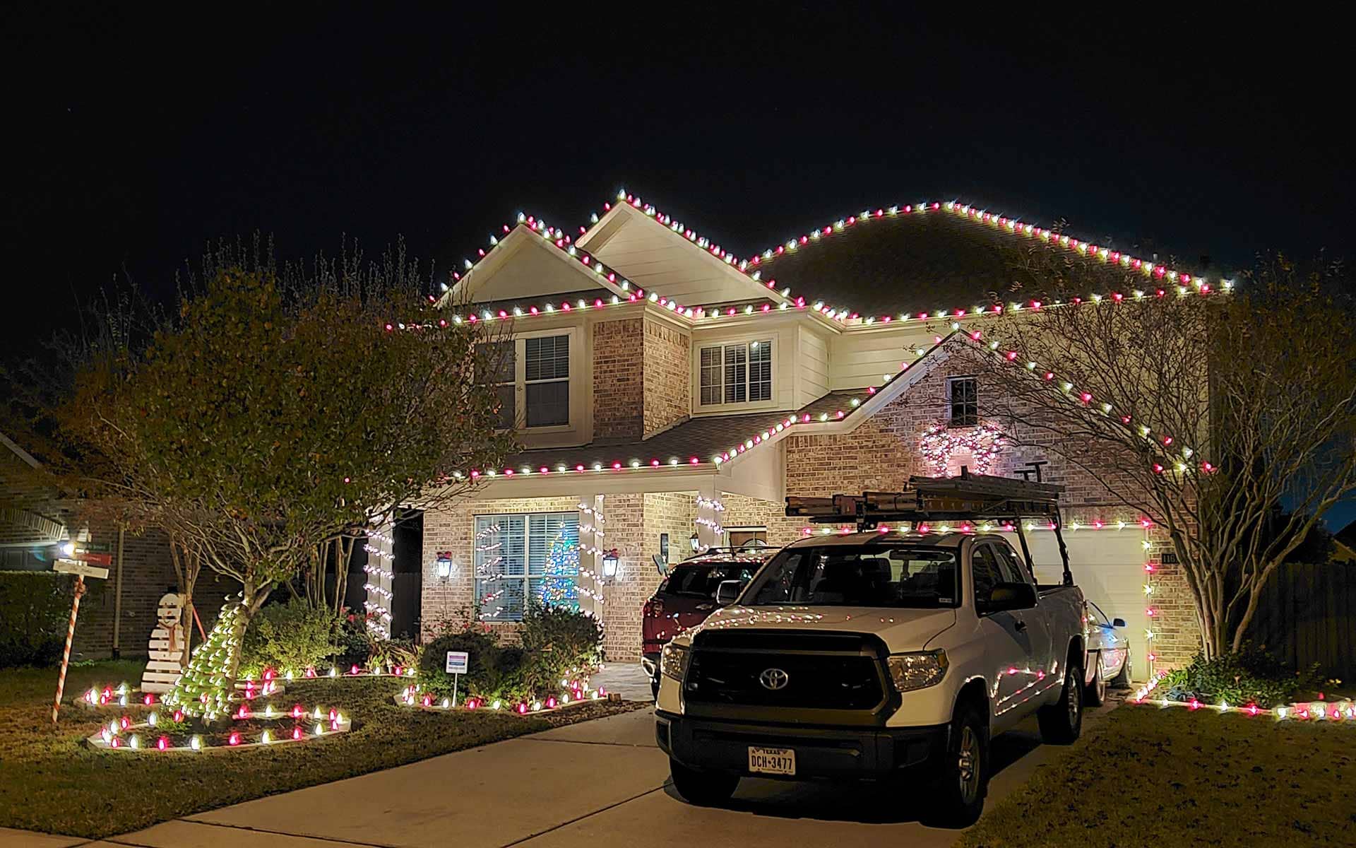 Red and white Christmas lights on a two-story brick home with lit walkway and yard decorations