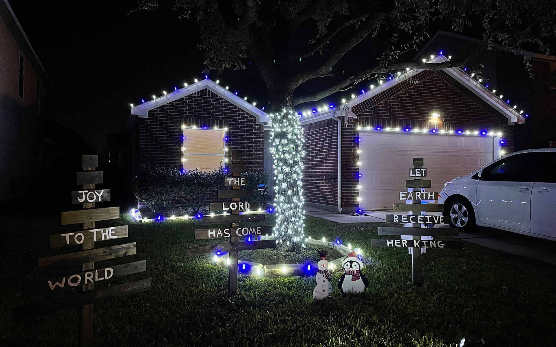 Christmas light display with a lit tree and 'Joy to the World' yard signs at a Tomball-area home