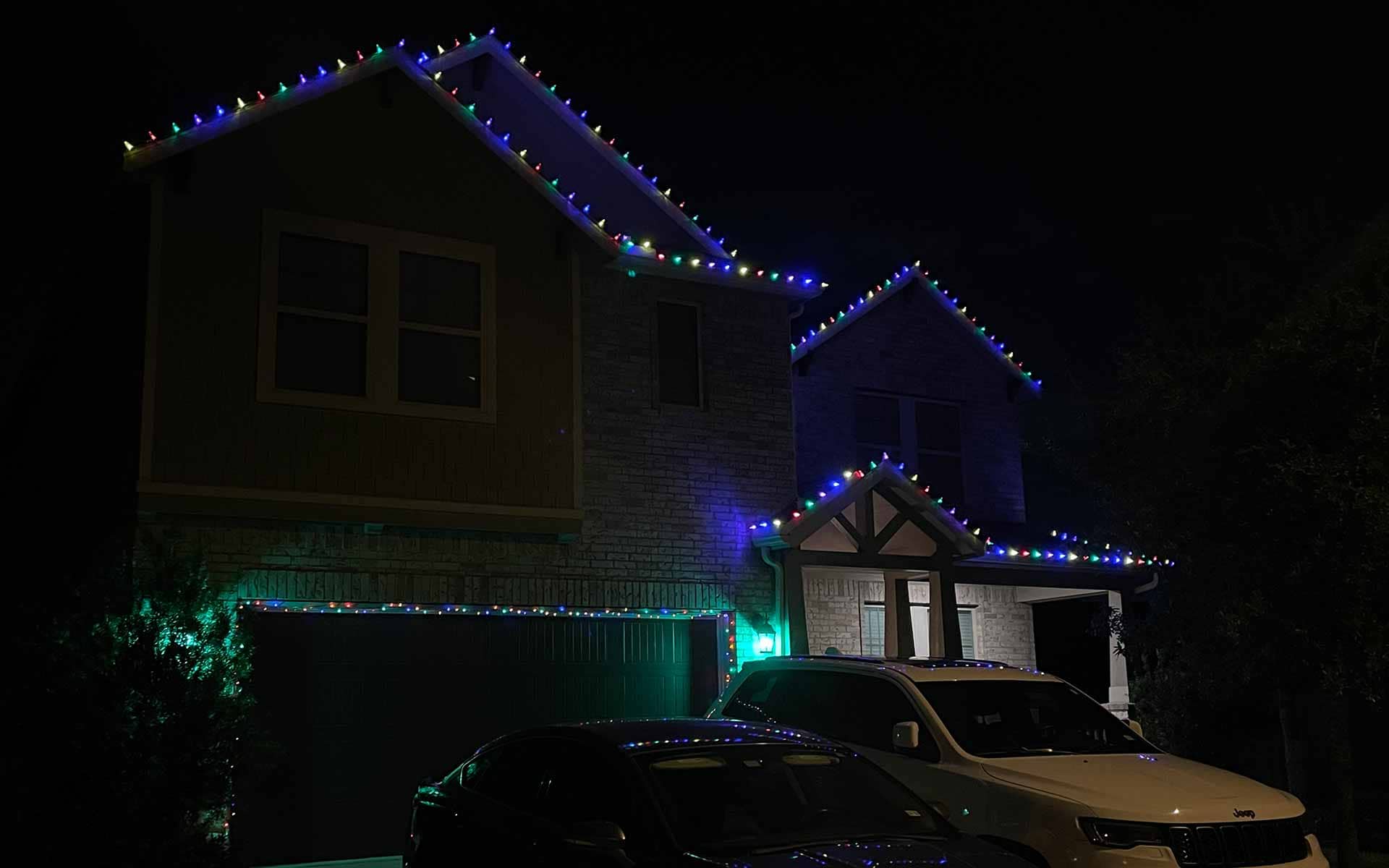 Multicolor Christmas lights lining the rooflines of a two-story North Houston home at night