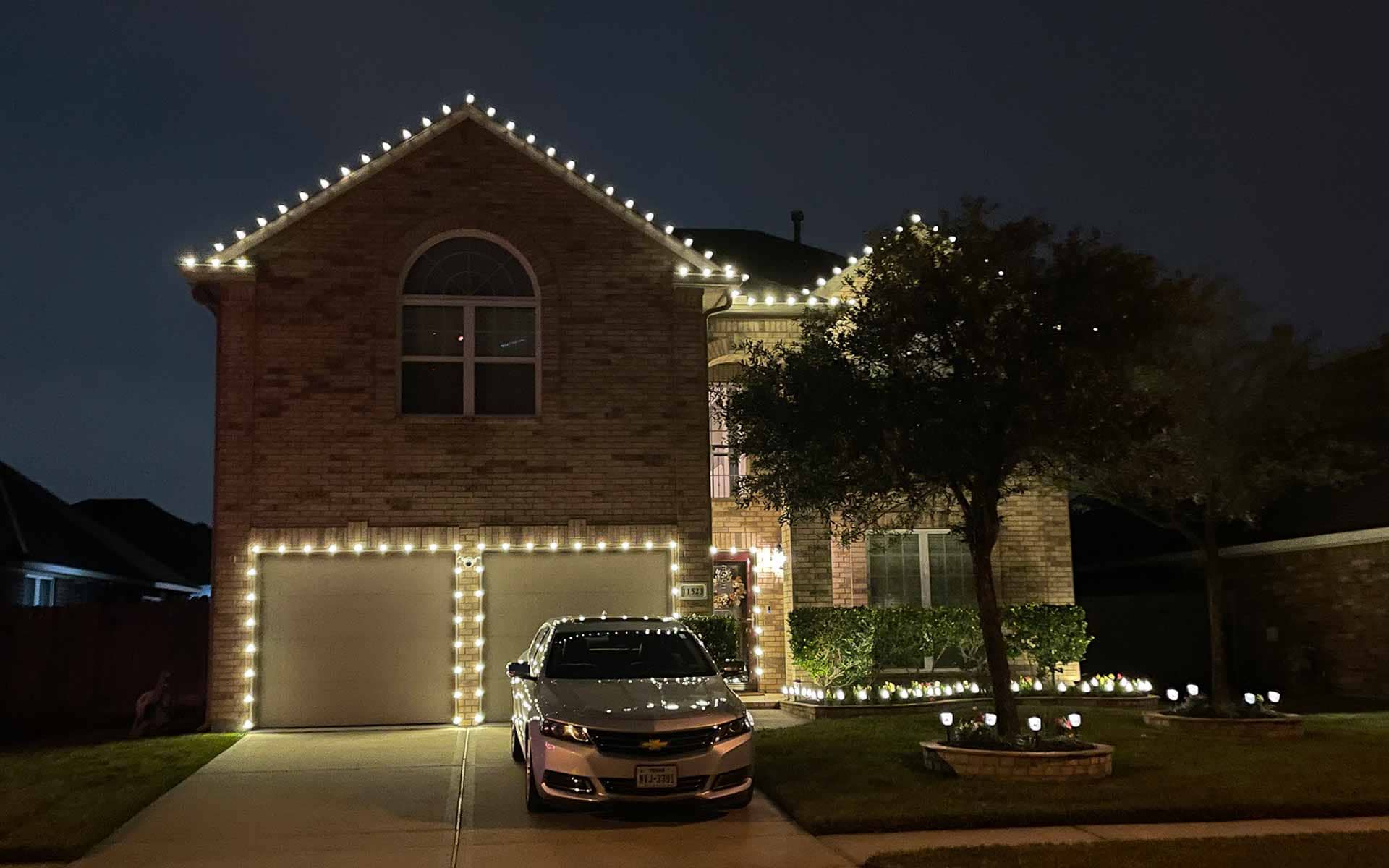 Warm white Christmas lights framing a brick home's roofline and garage against the night sky
